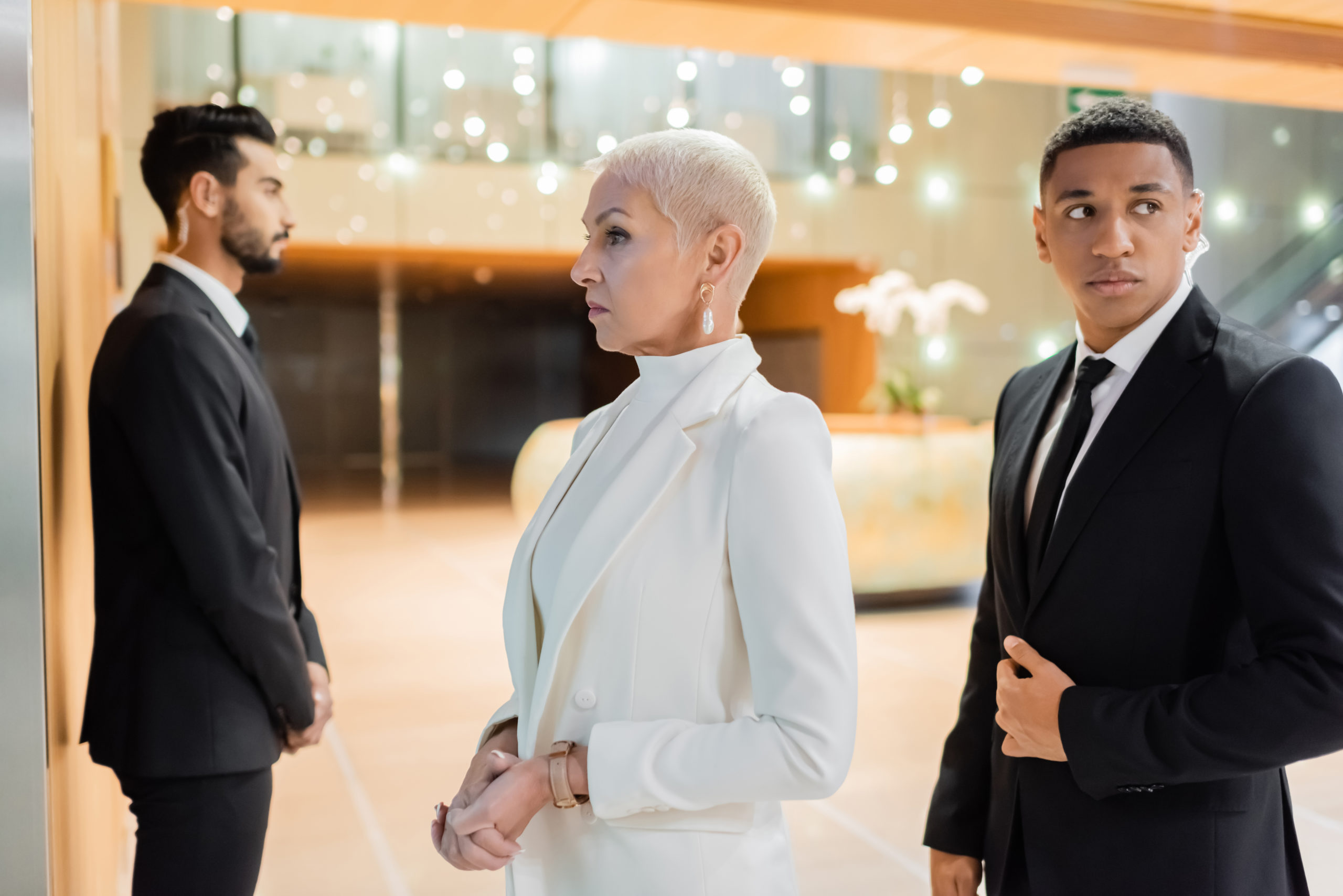 multiethnic guards escorting senior businesswoman in hotel foyer during business trip,stock image